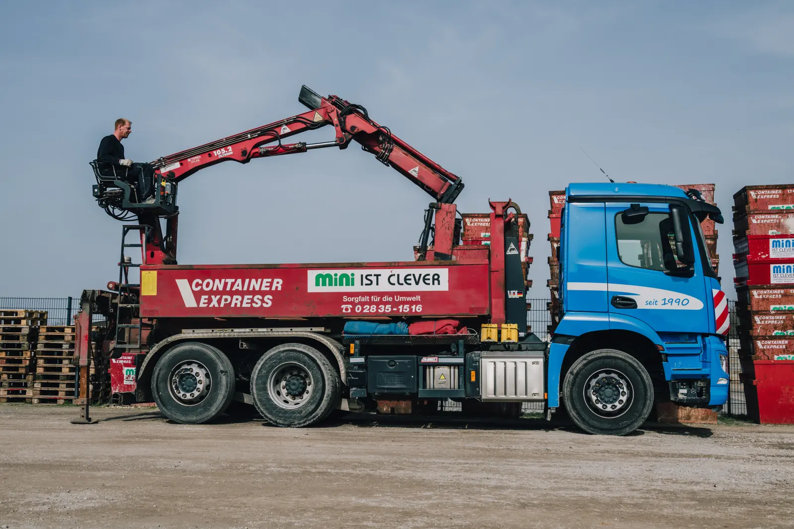 Blauer Container-Lkw mit rotem Ladekran und Fahrer.